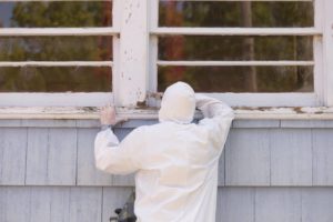 Worker inspecting an older building exterior where asbestos-containing materials may be present