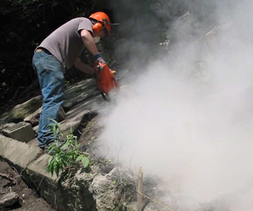 Worker cutting concrete and generating a large visible cloud of construction dust