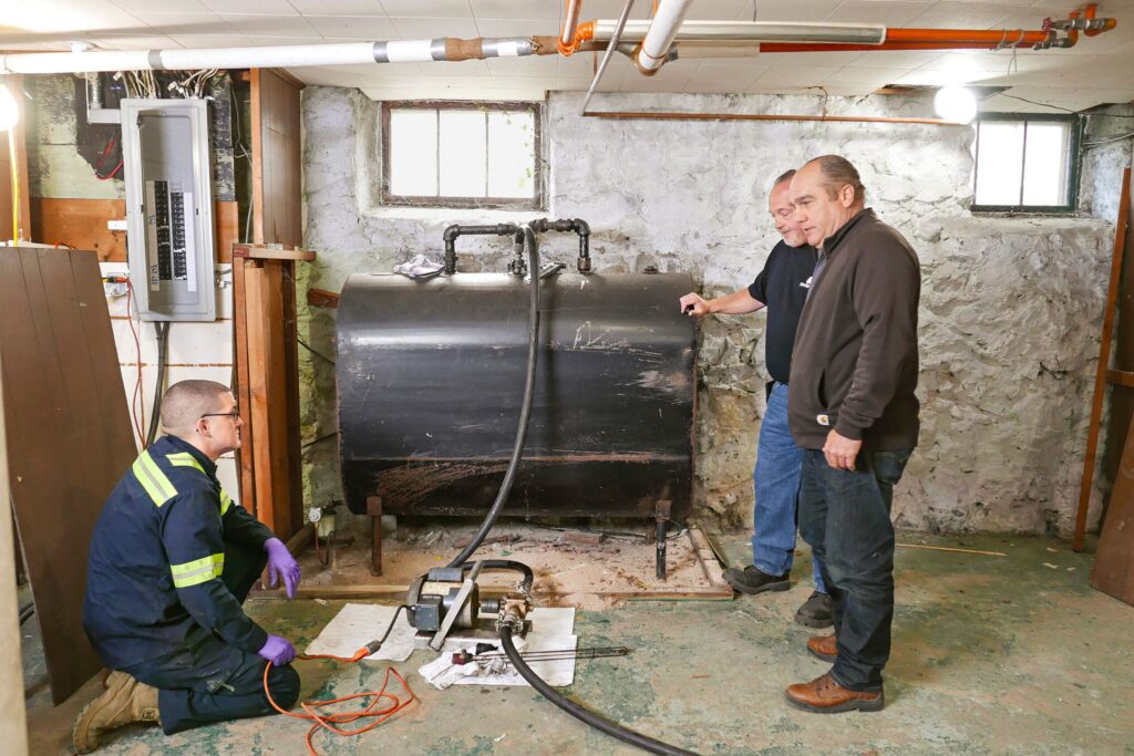Environmental professionals evaluating a heating oil tank and leak-testing equipment during a property assessment
